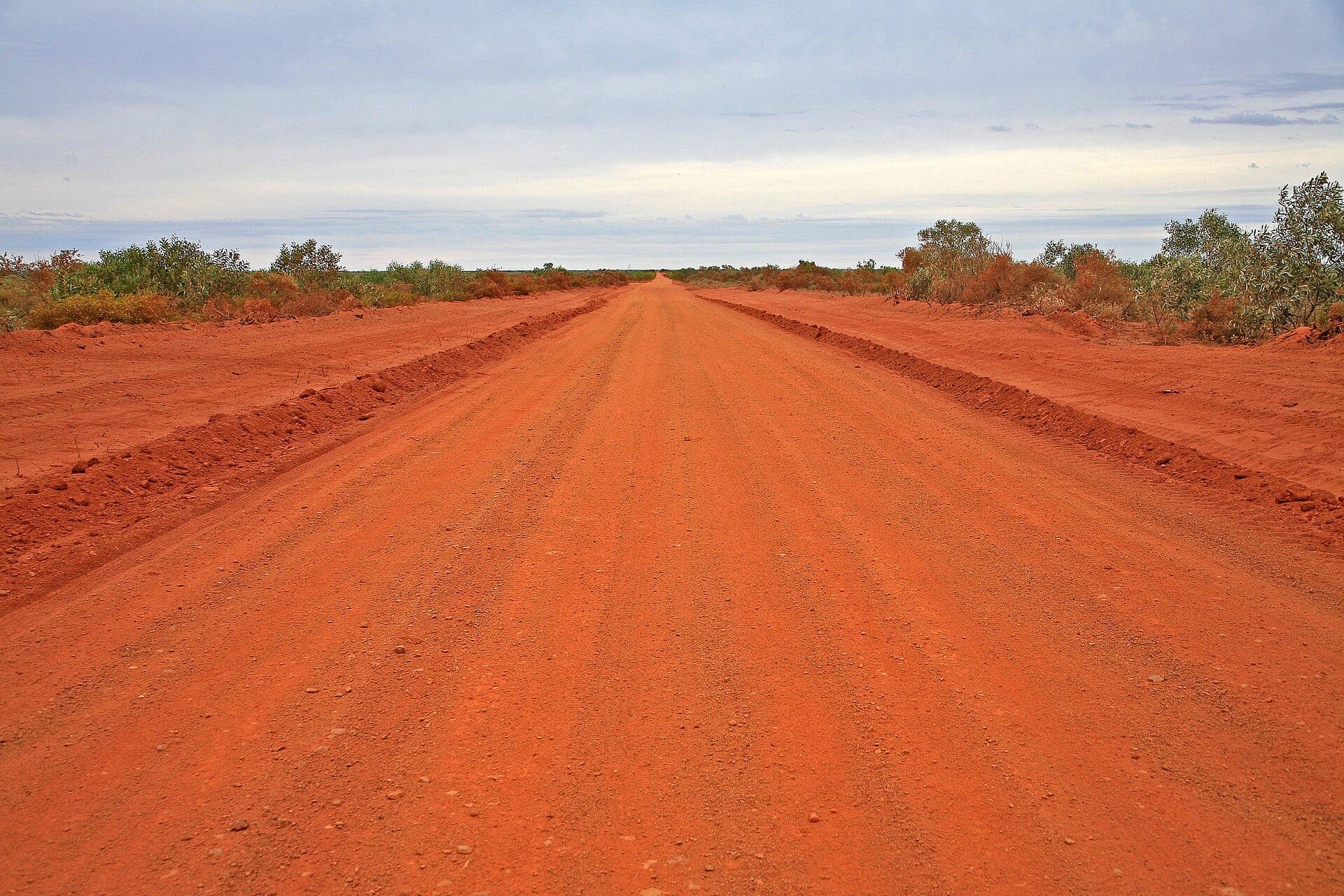 A red dirt road running straight to the horizon through outback scrub.