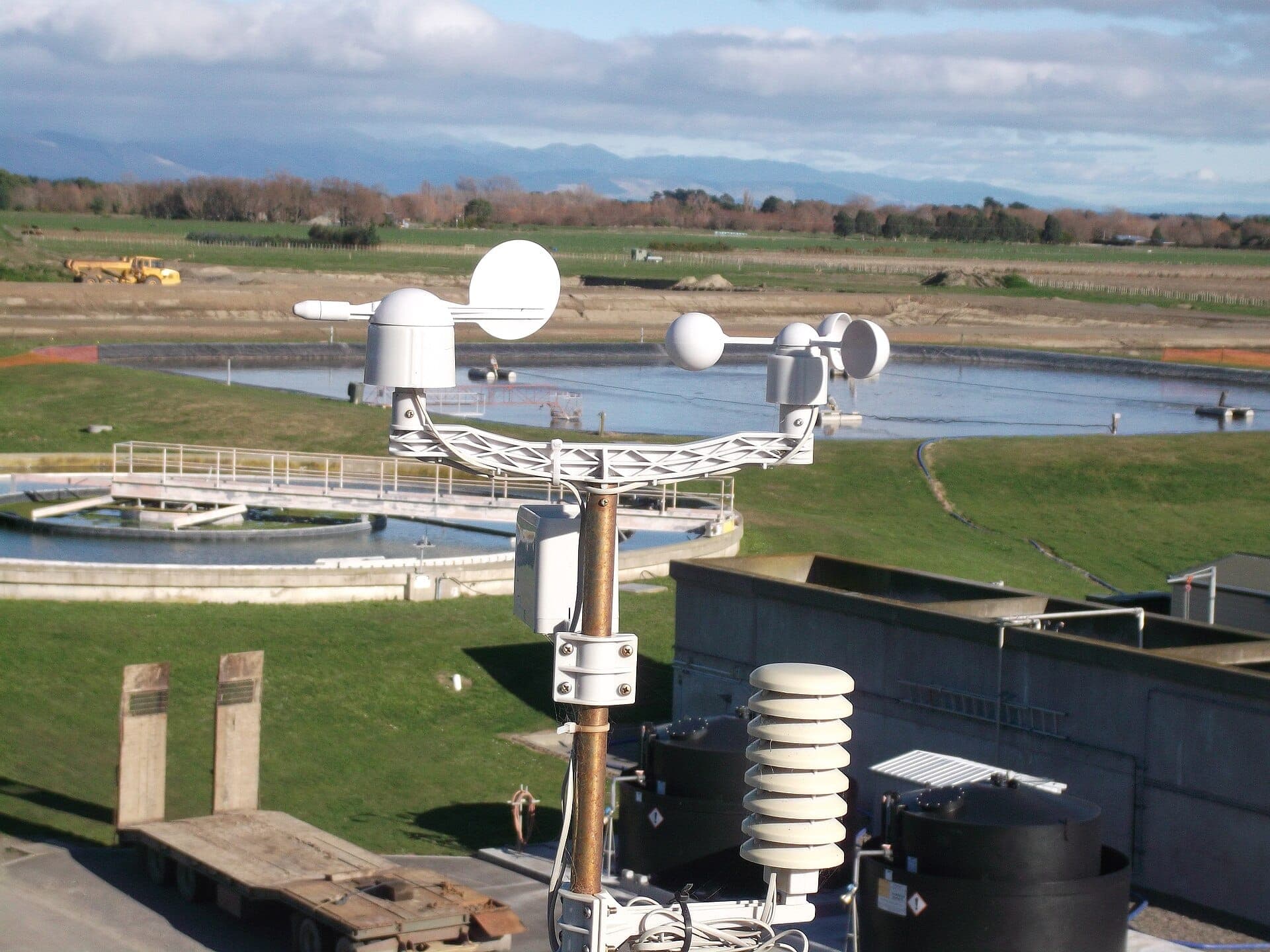 A weather station with sensors on a mast above water treatment ponds.